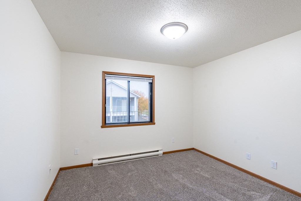 an empty living room with carpet and a window. Fargo, ND Flagstone Apartments