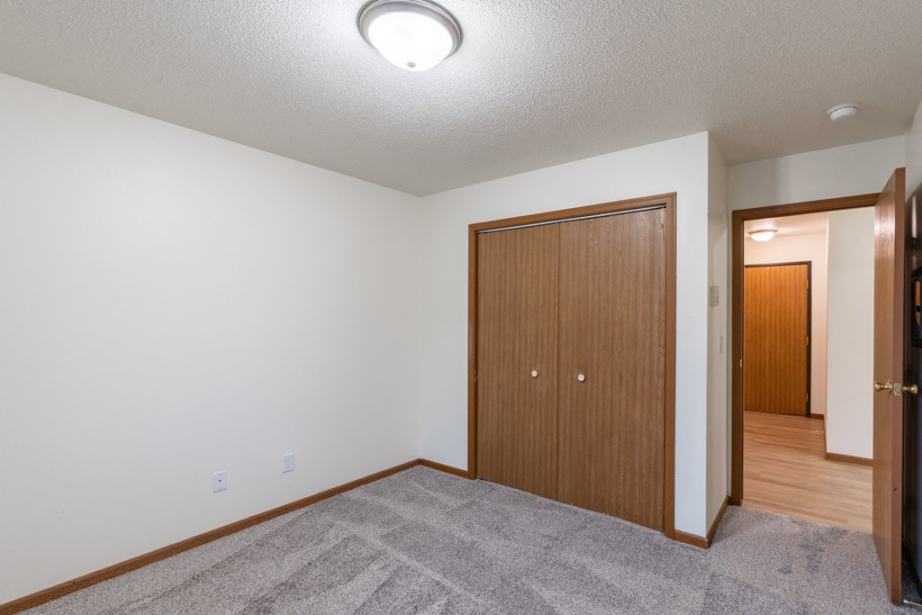a living room with carpet and a door to a hallway with a closet. Fargo, ND Flagstone Apartments