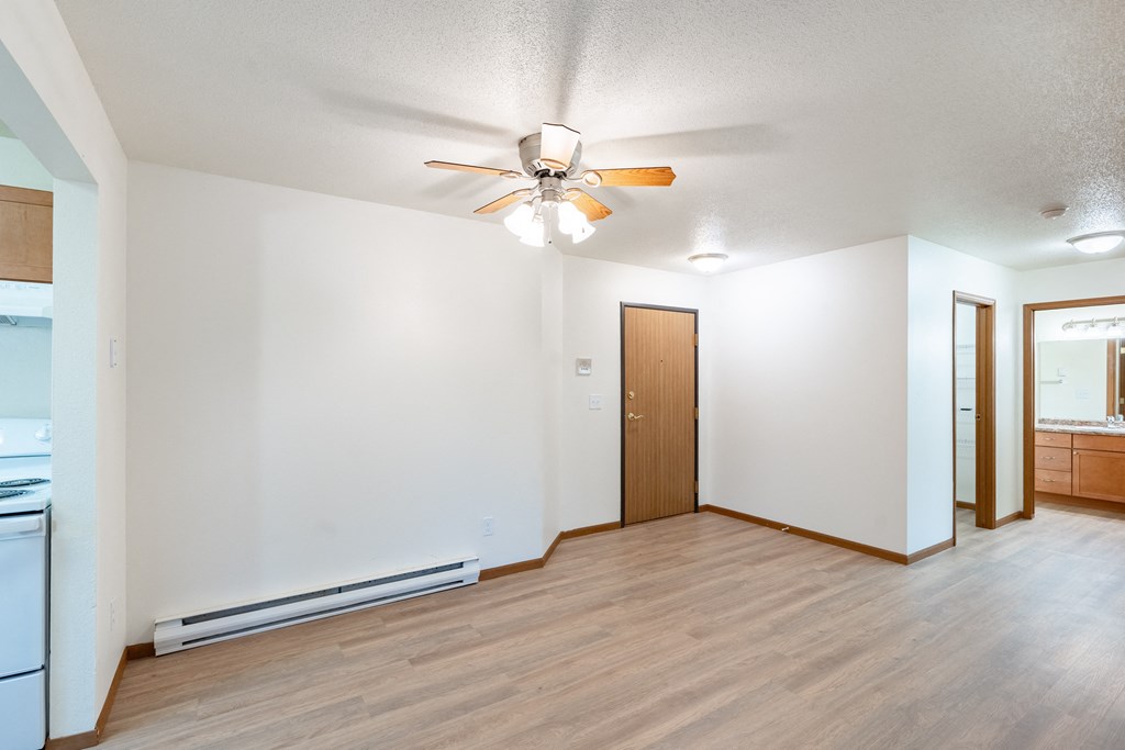 an empty living room with a ceiling fan and a kitchen. Fargo, ND Flagstone Apartments