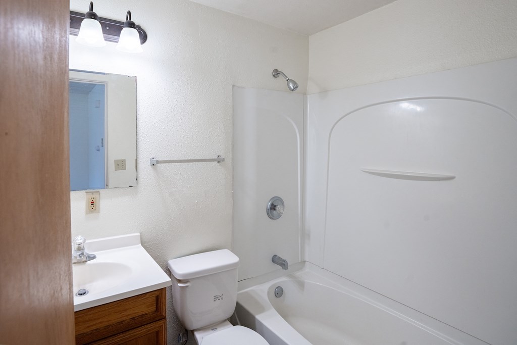a bathroom with a shower toilet and sink and a mirror. Fargo, ND Forest Avenue Apartments