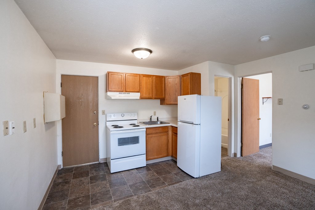 an empty kitchen with white appliances and wooden cabinets.Fargo, ND Forest Avenue Apartments