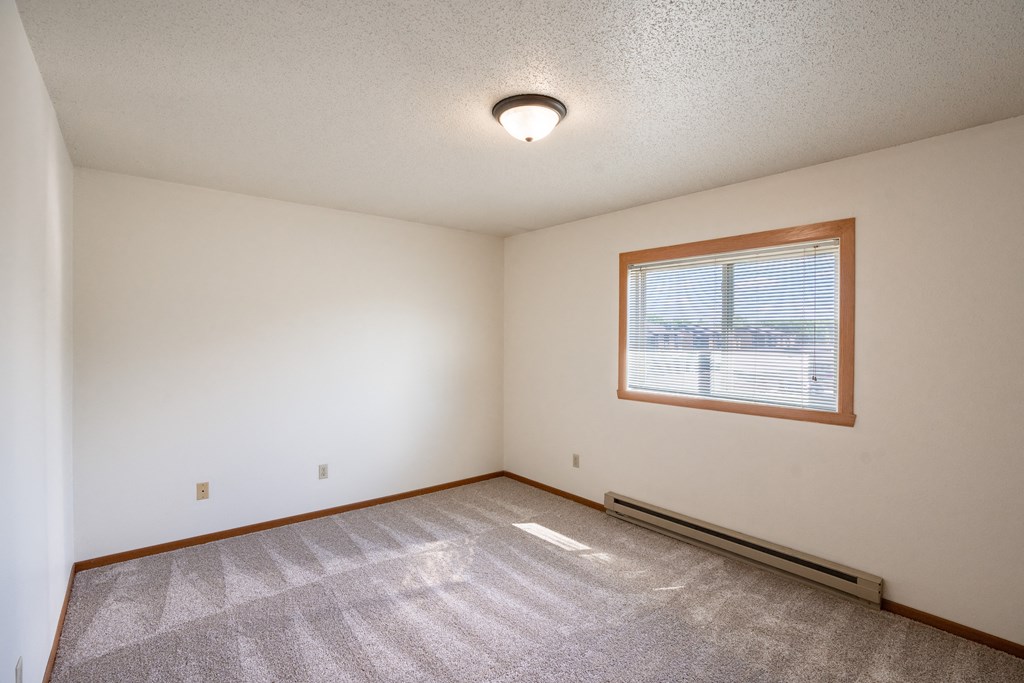 the living room of an empty house with a window and a carpet. Fargo, ND Hunters Run 2 Apartments