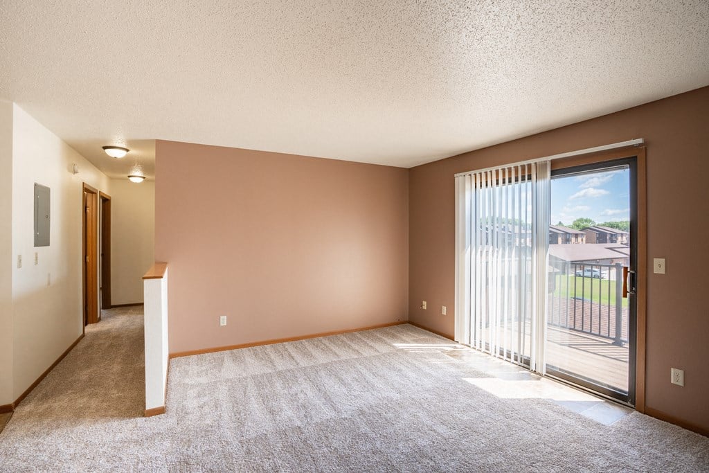 an empty living room with a sliding glass door to a balcony. Fargo, ND Hunters Run 2 Apartments