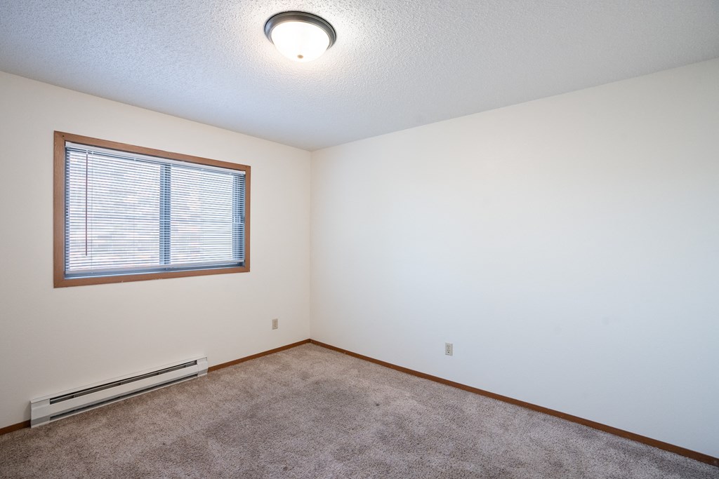 the living room of an empty house with carpet and a window. Fargo, ND Kentwood Manor Apartments