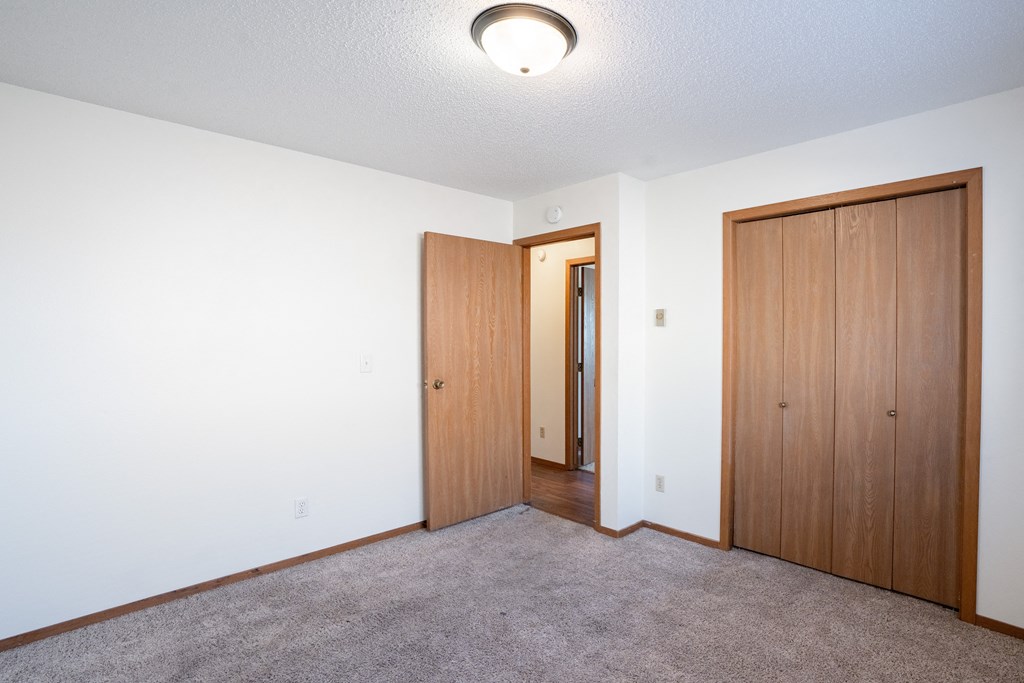 an empty living room with a door to a hallway and a closet. Fargo, ND Kentwood Manor Apartments