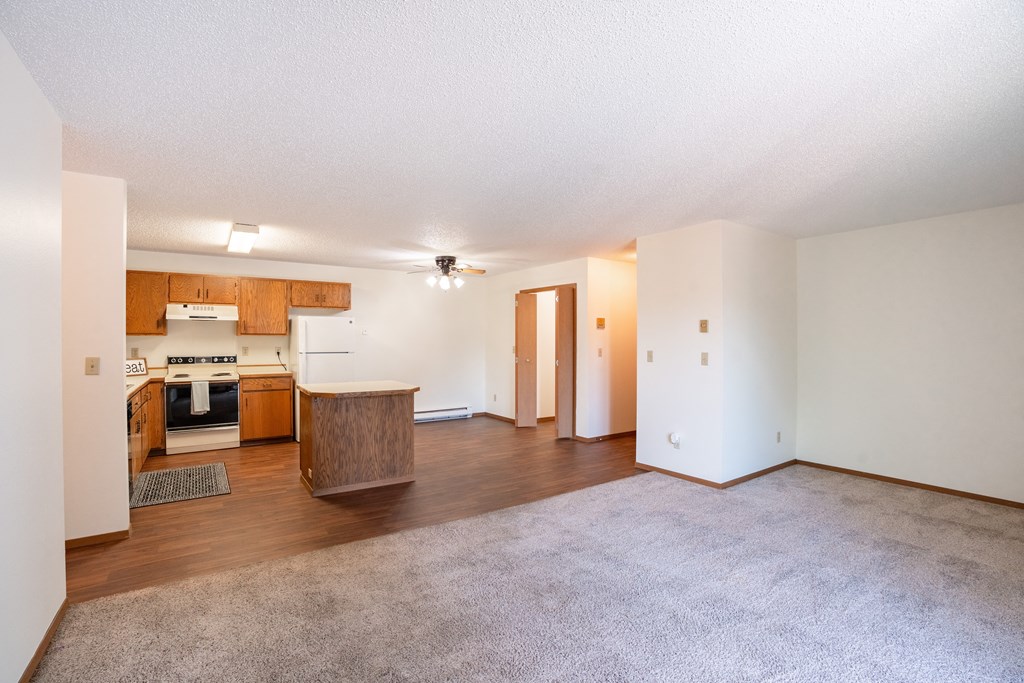 the living room and kitchen of an apartment with white walls and wood flooring. Fargo, ND Kentwood Manor Apartments