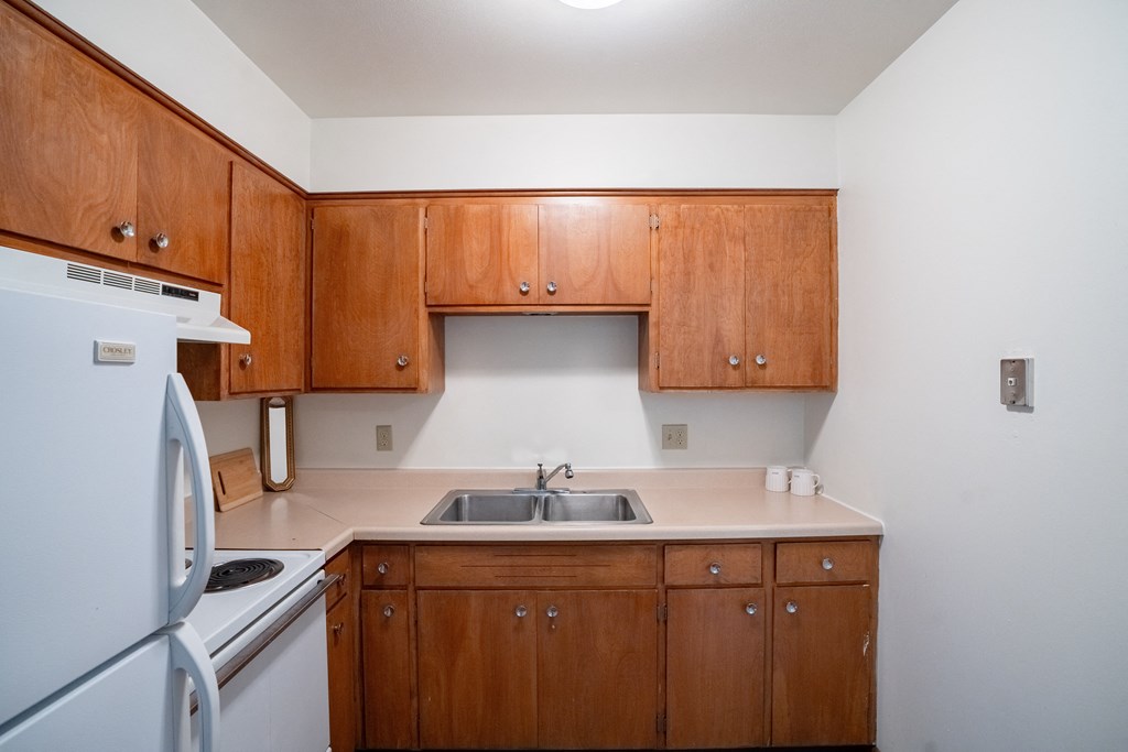 an empty kitchen with wooden cabinets and a white stove and refrigerator. Fargo, ND Luxford Apartments