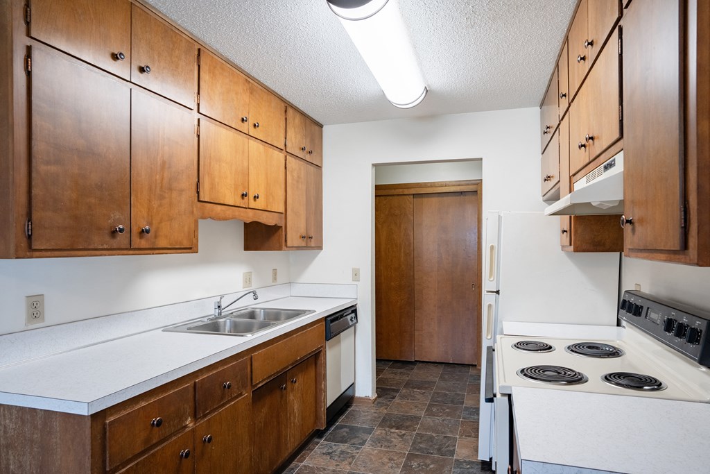 an empty kitchen with white appliances and wooden cabinets. Fargo, ND Martha Alice Apartments | 21B
