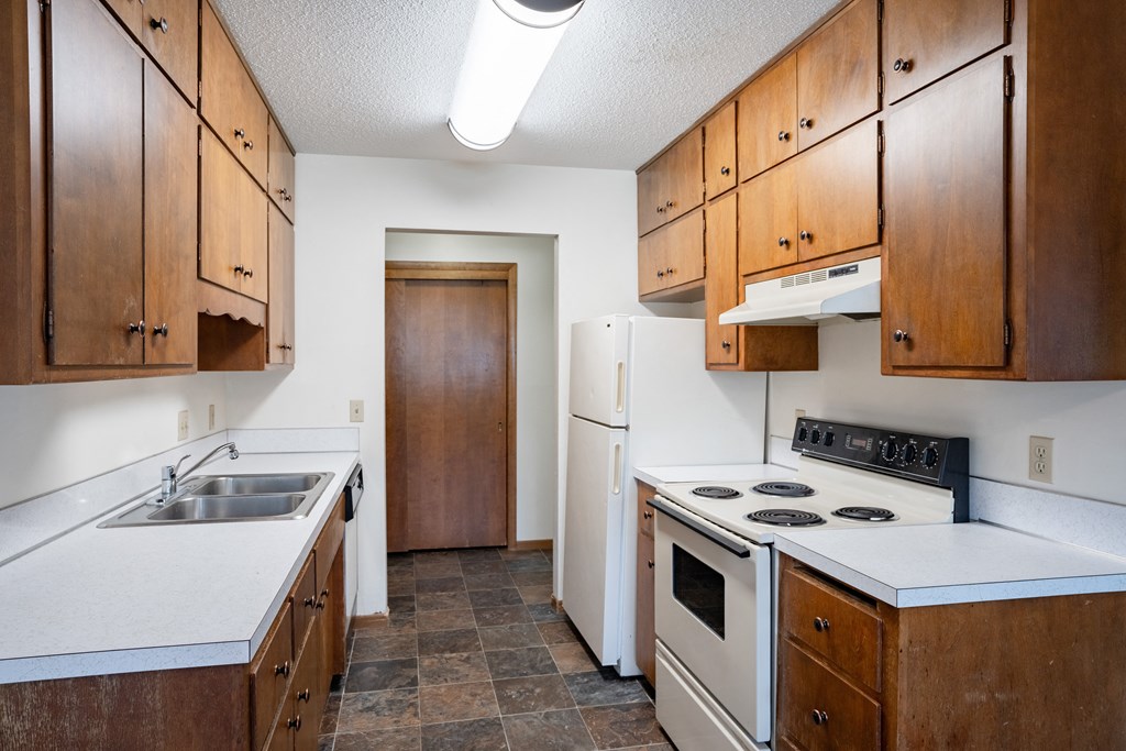 an empty kitchen with white appliances and wooden cabinets. Fargo, ND Martha Alice Apartments