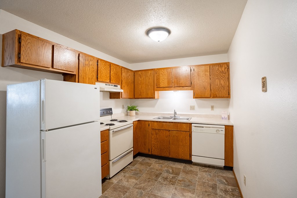a small kitchen with white appliances and wooden cabinets. Fargo, ND Monticello Apartments