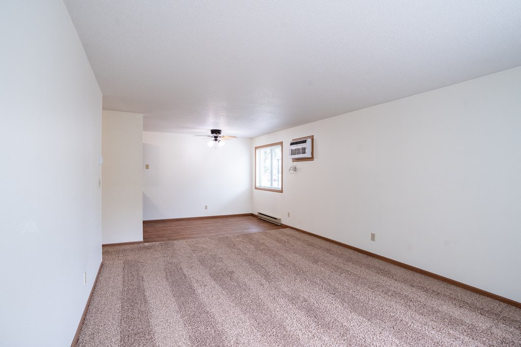 the living room and dining room of an apartment with carpet and white walls. Fargo, ND Monticello Apartments