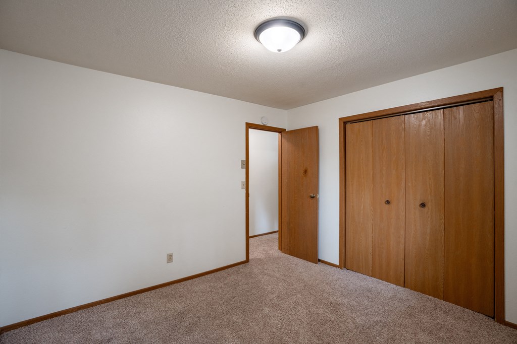 a bedroom with carpet and a door to a closet. Fargo, ND Monticello Apartments