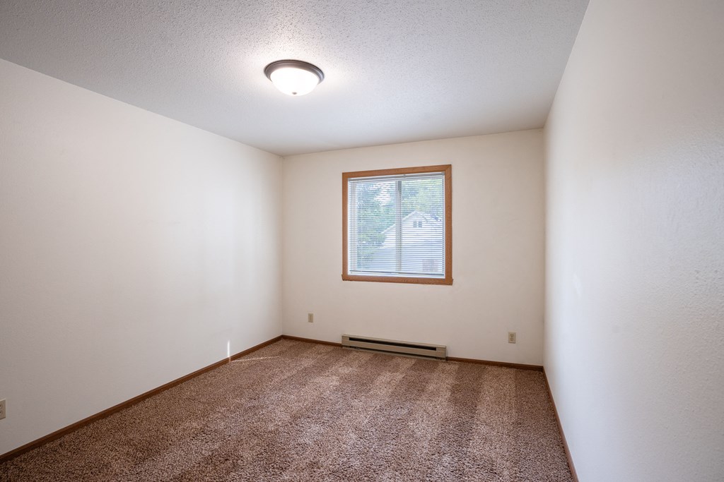 an empty living room with carpet and a window. Fargo, ND Monticello Apartments