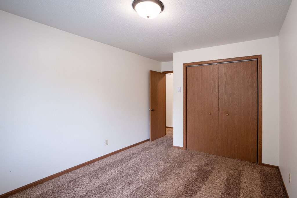 an empty living room with carpet and a door to a closet. Fargo, ND Monticello Apartments