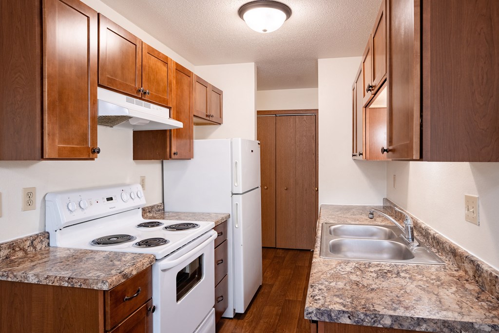 a kitchen with white appliances and wooden cabinets and granite counter tops. Fargo, ND Monticello Apartments