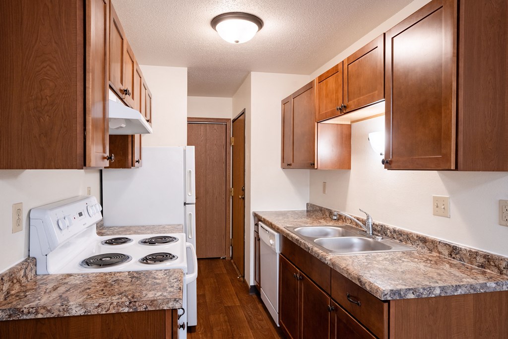 a kitchen with wood cabinets and white appliances and granite counter tops. Fargo, ND Monticello Apartments
