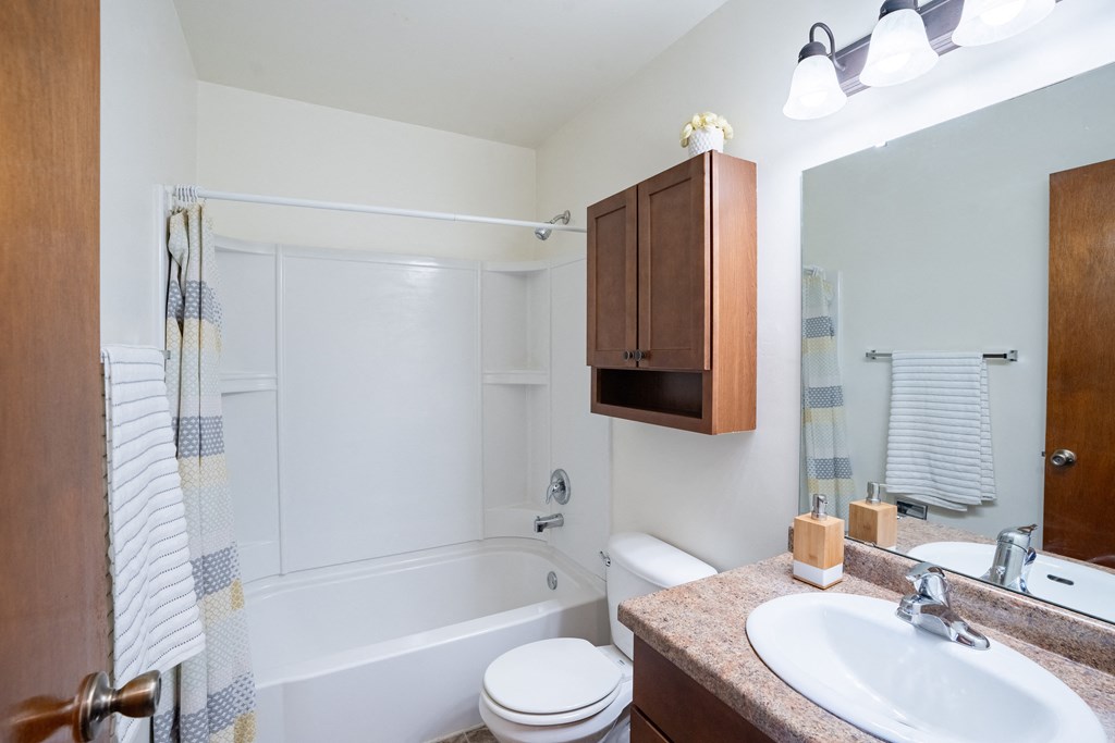 a bathroom with a sink toilet and shower and a mirror. Fargo, ND Morningside Apartments
