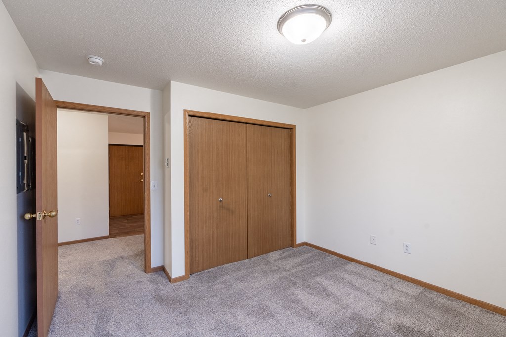 an empty living room with a door to a bedroom and a closet. Fargo, ND Oxford Apartments