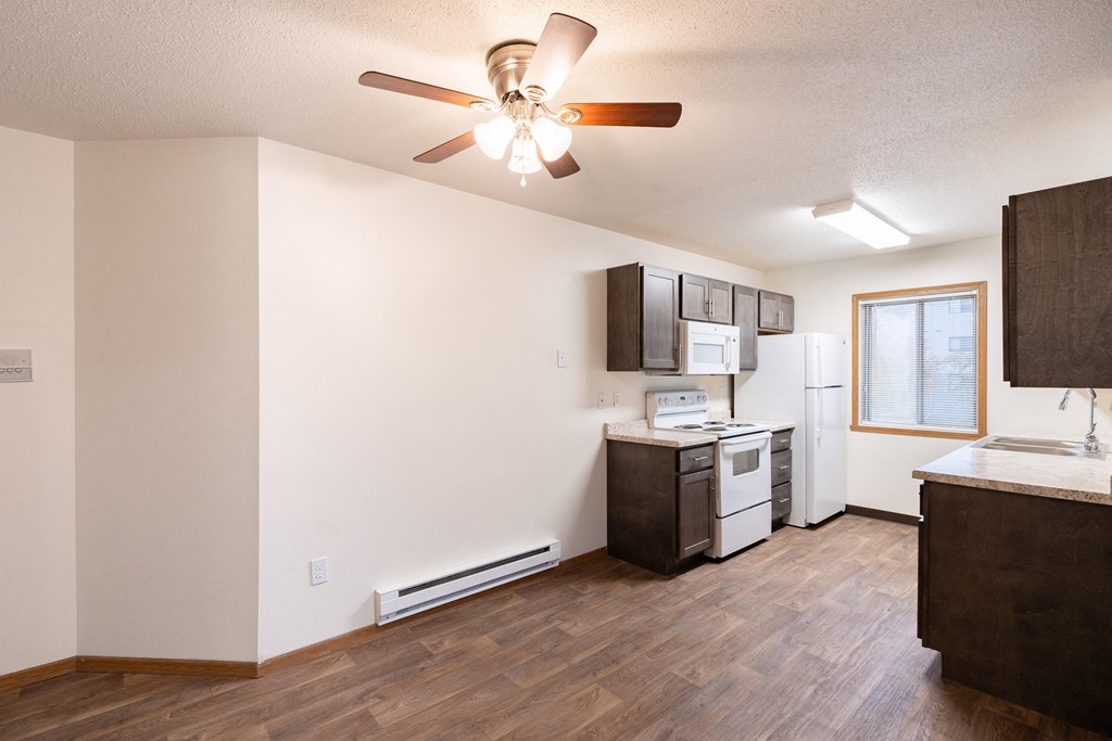 an empty living room with a kitchen and a ceiling fan. Fargo, ND Oxford Apartments