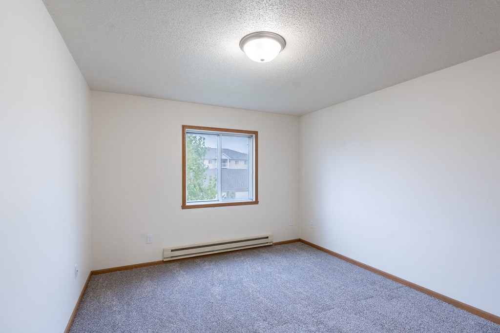 the living room of an empty room with carpet and a window. Fargo, ND Oxford Apartments
