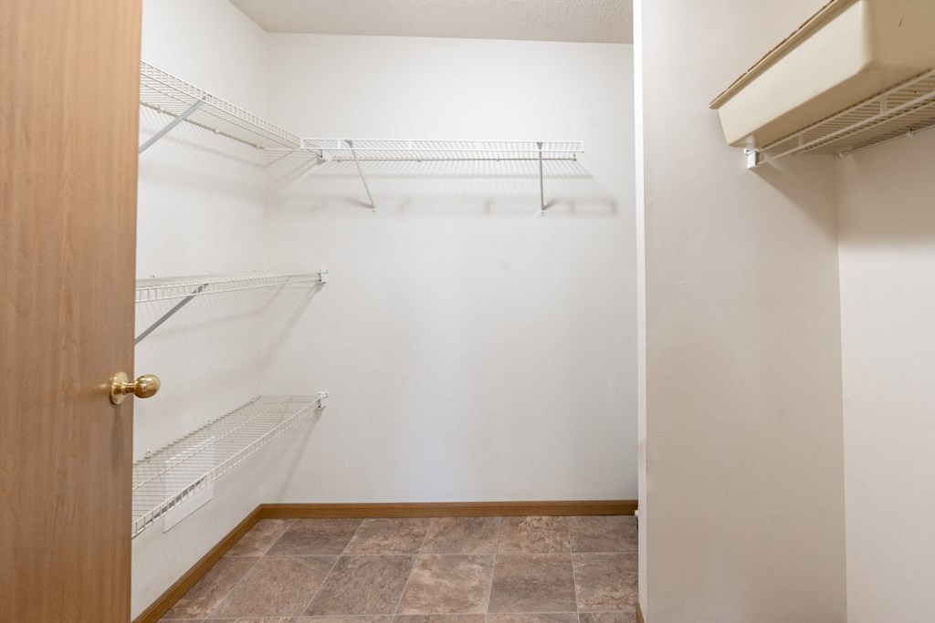 an empty closet with white walls and an open door to a white closet with shelves. Fargo, ND Oxford Apartments