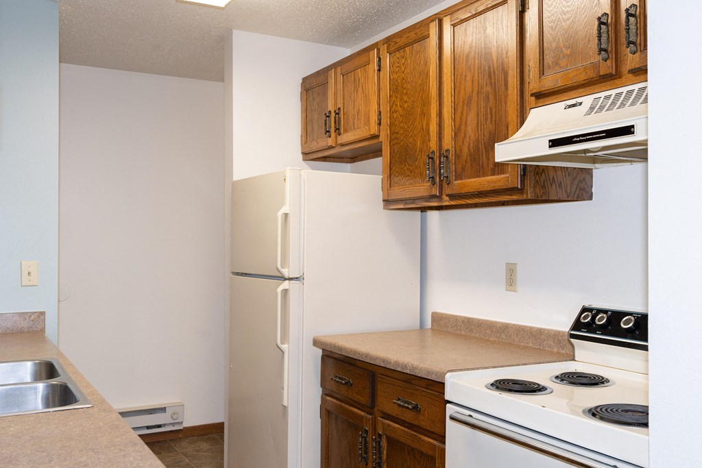 a kitchen with white appliances and wooden cabinets and a refrigerator. Fargo, ND Pacific South Apartments