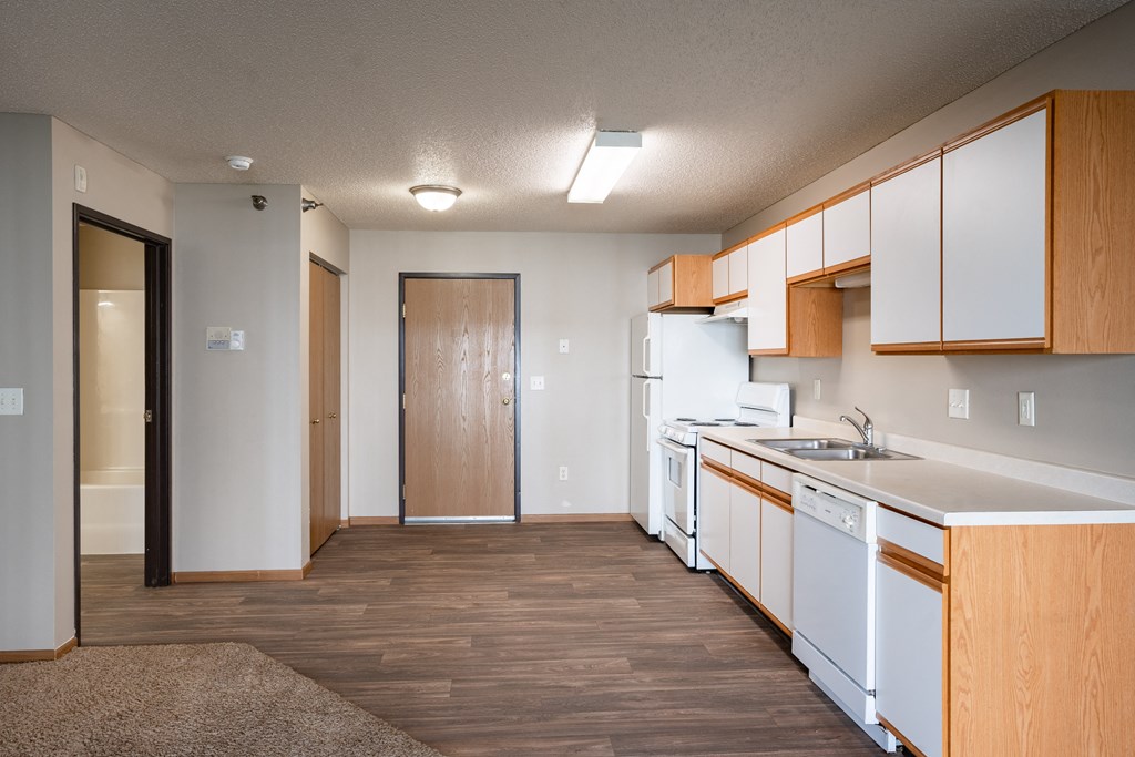 an empty kitchen with white appliances and wood flooring and a door to the bathroom