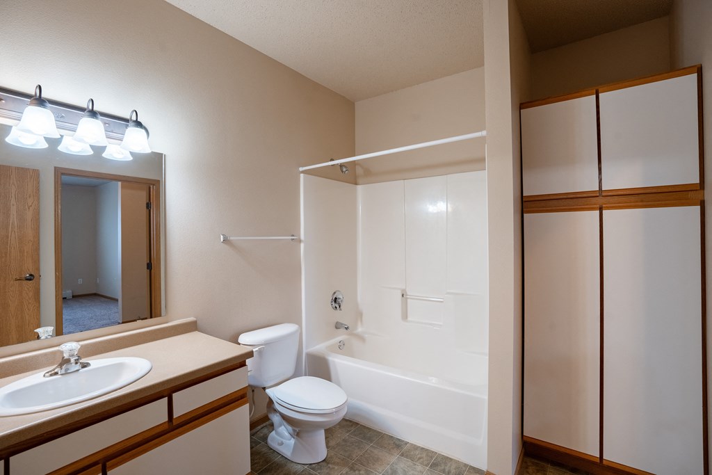 a bathroom with a shower toilet and sink and a mirror. Fargo, ND West Lake Apartments