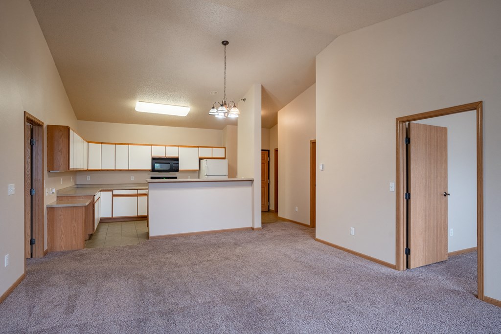 an empty living room and kitchen with an open door. Fargo, ND West Lake Apartments