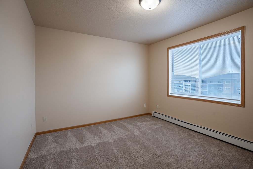 a bedroom with a large window and carpet. Fargo, ND West Lake Apartments