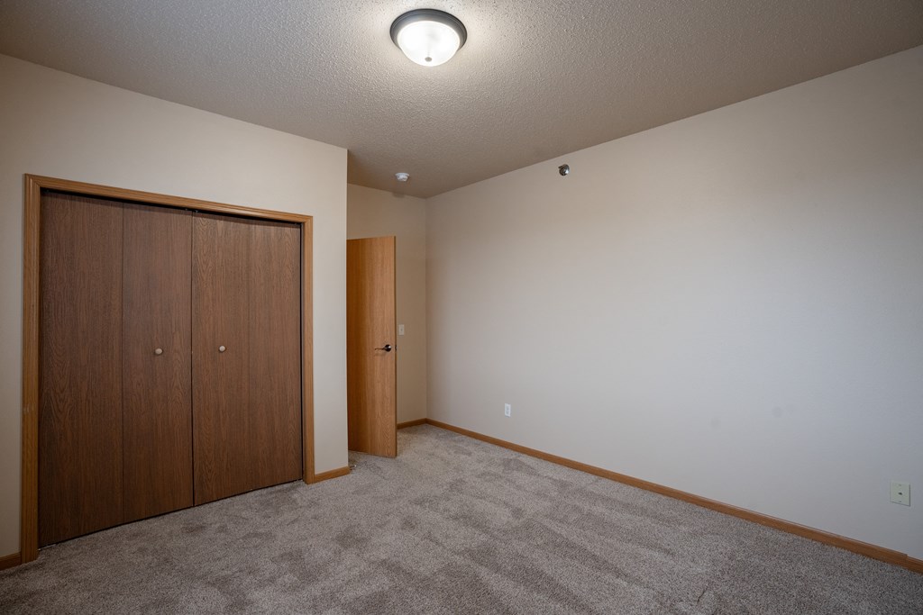 an empty room with carpet and a door to a closet. Fargo, ND West Lake Apartments