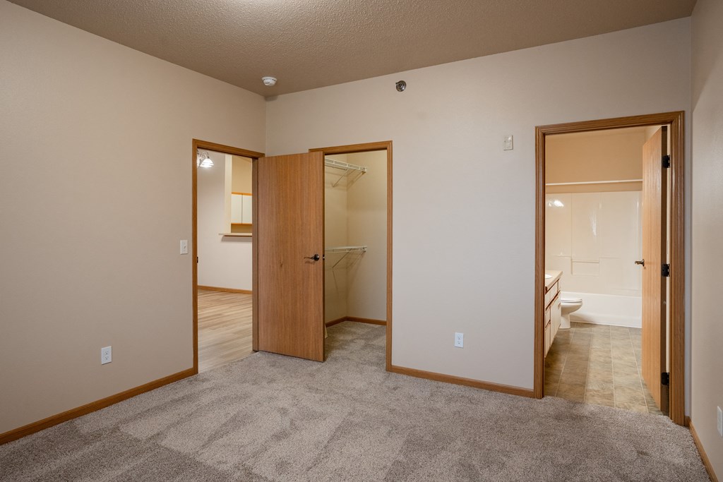 a bedroom with two doors to a bathroom and a closet. Fargo, ND West Lake Apartments