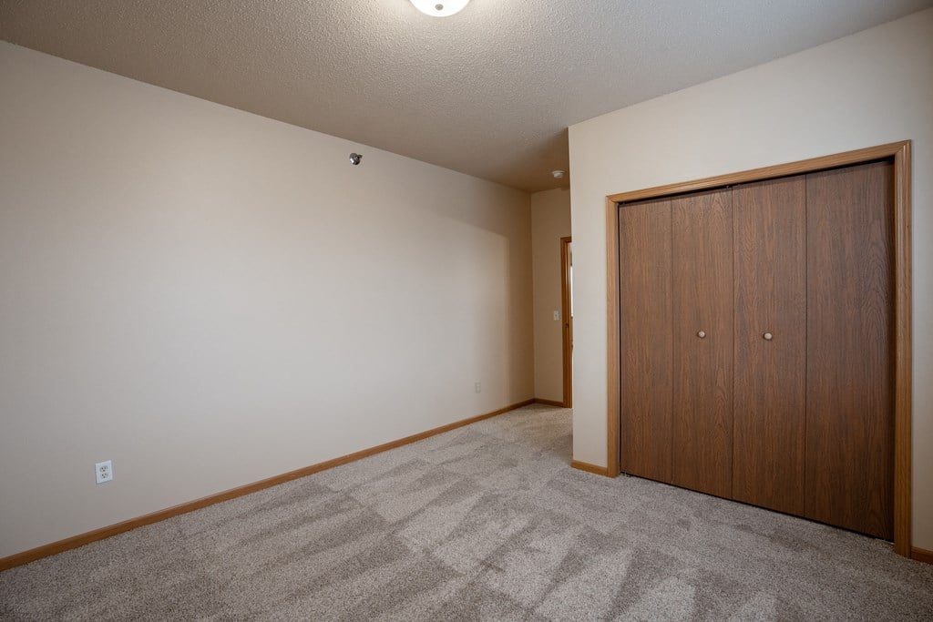 a bedroom of an empty apartment with a door to a closet. Fargo, ND West Lake Apartments