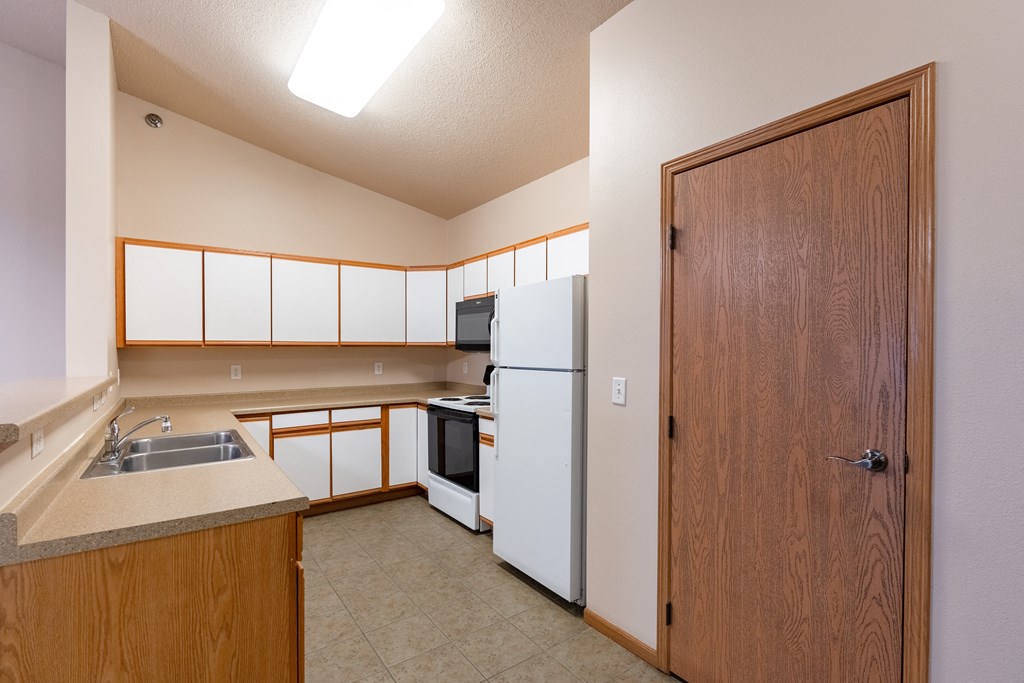 a kitchen with white appliances and a wooden door. Fargo, ND West Lake Apartments