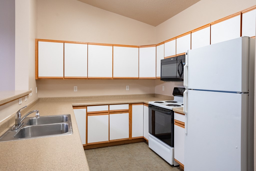 an empty kitchen with white cabinets and a refrigerator and sink. Fargo, ND West Lake Apartments