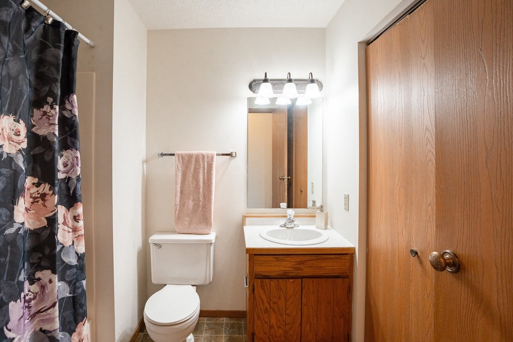 a bathroom with a shower curtain and a toilet and sink. Fargo, ND Westview Towers Apartments