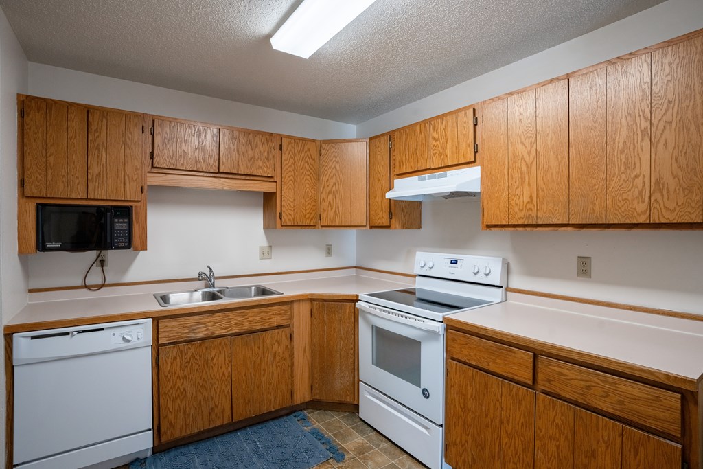 Fargo, ND Westview Towers Apartments | Kitchen an empty kitchen with white appliances and wooden cabinets. Fargo, ND Westview Towers Apartments
