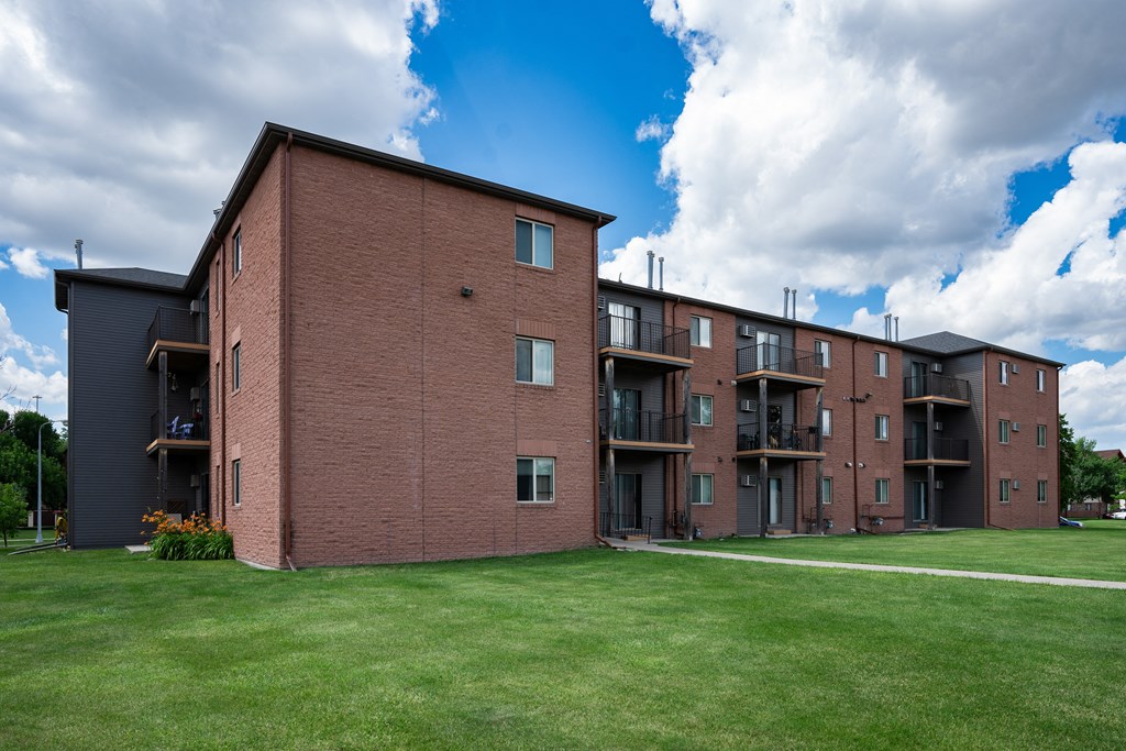 a large brick apartment building with a green lawn