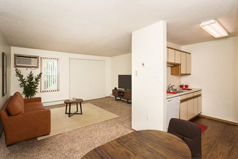 Grand Forks, ND Bristol Park Apartments. a living room with a couch a table and a chair and a kitchen with a sink and