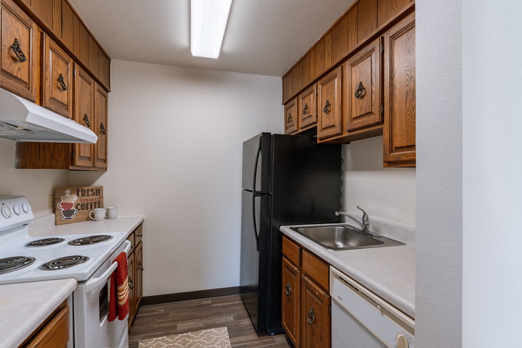 a kitchen with white appliances and wooden cabinets and a black refrigerator. Grand Forks, ND Cedarwood Apartments