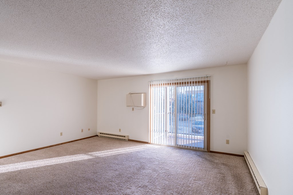 an empty living room with a sliding glass door to a balcony. Grand Forks, ND Cedarwood Apartments