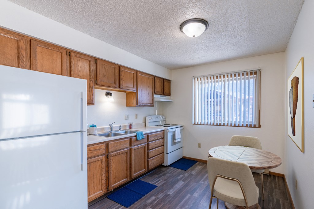 a kitchen with a dining table and a refrigerator. Grand Forks, ND Chandler 1898 Apartments