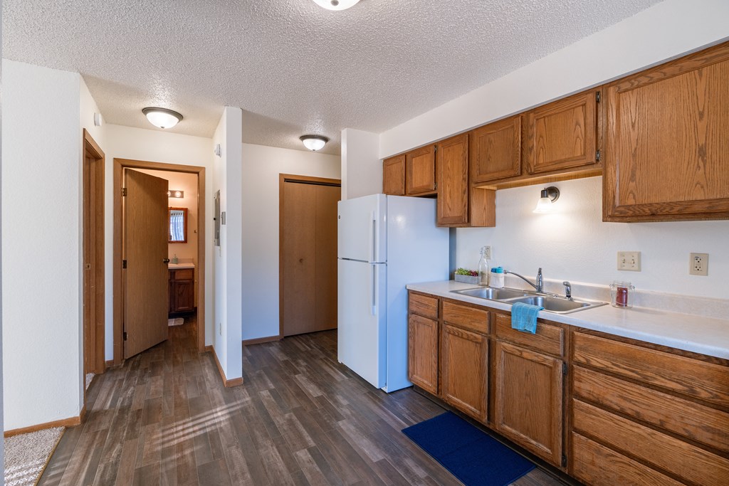 a kitchen with wooden cabinets and a white refrigerator and a door. Grand Forks, ND Chandler 1866 Apartments