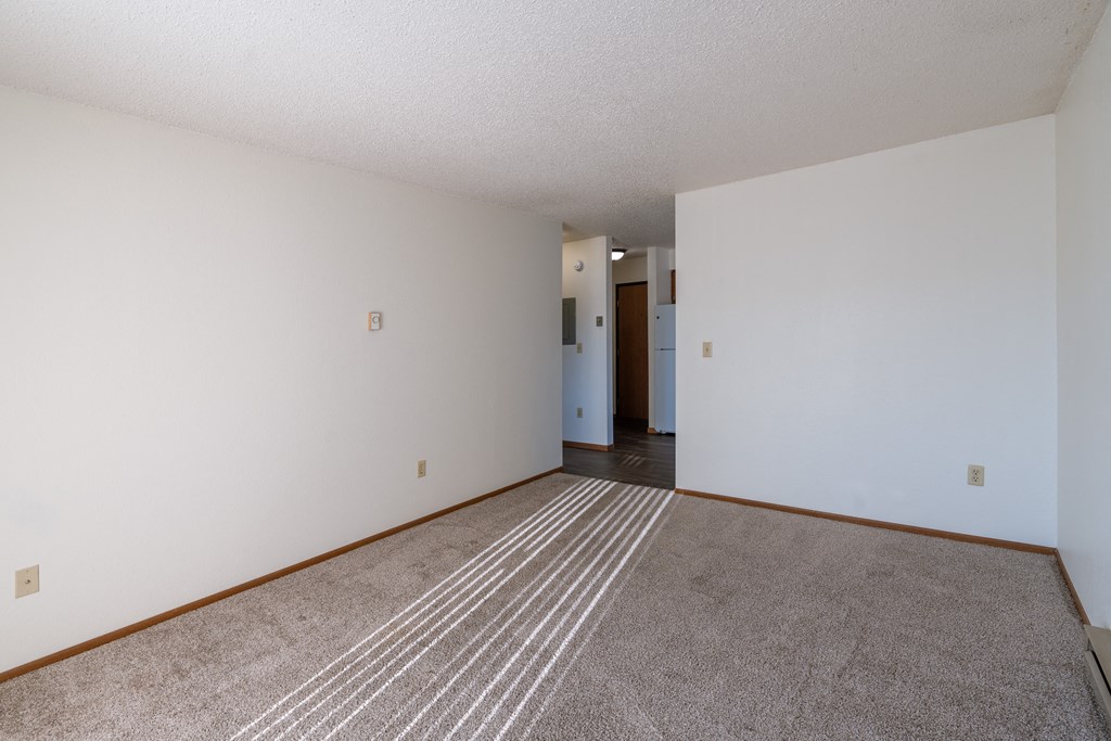 an empty living room with carpet and white walls. Grand Forks, ND Chandler 1866 Apartments