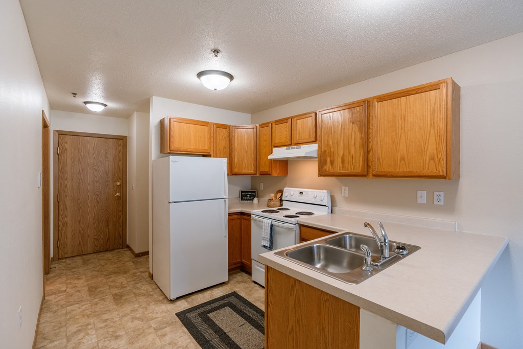 Grand Forks, ND Creekside Apartments. A kitchen with white appliances and wooden cabinets and a sink