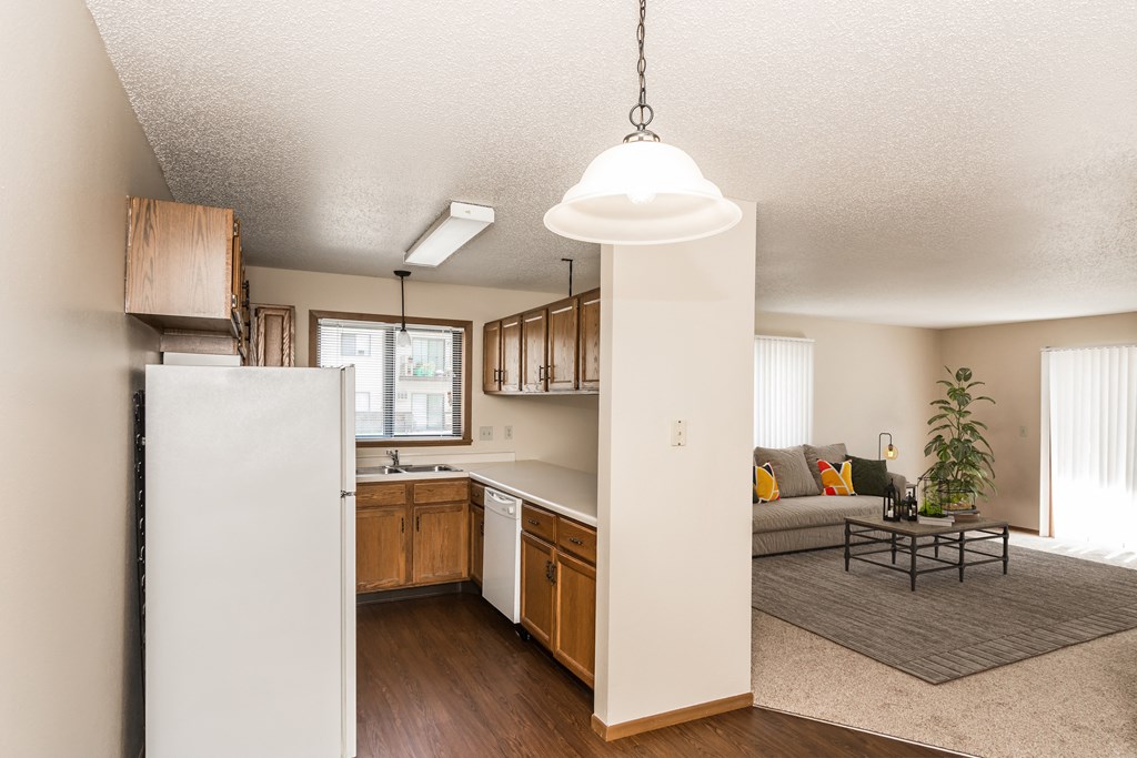 Grand Forks Harrison and Richfield Apartments. A kitchen with white appliances and living room with a couch and a coffee table in the background
