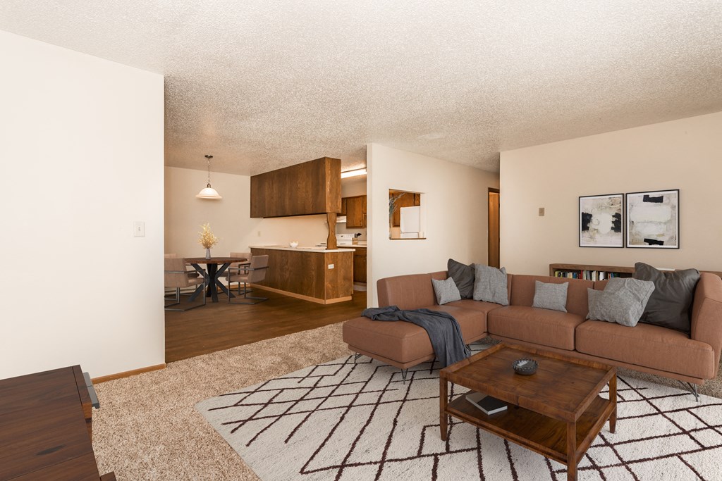 Grand Forks Kremer Apartments. A living room with a brown couch and a wooden coffee table with a kitchen and dining area in the background