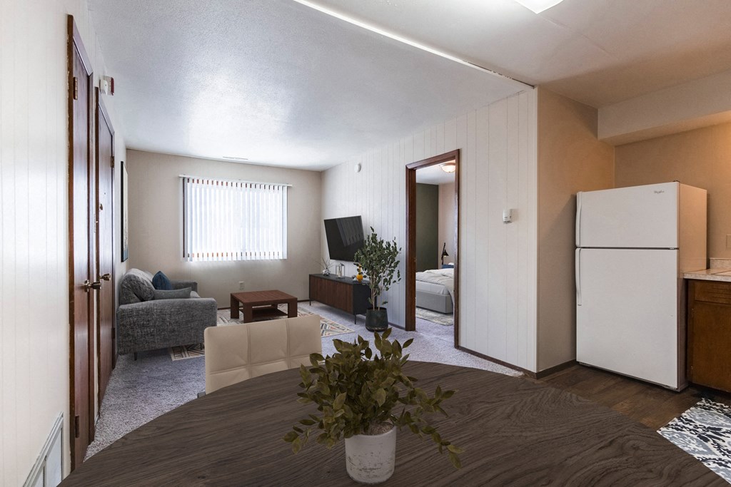 Grand Forks, ND Louise Apartments. A dining room with a table with a plant in front of it and a living room in the background