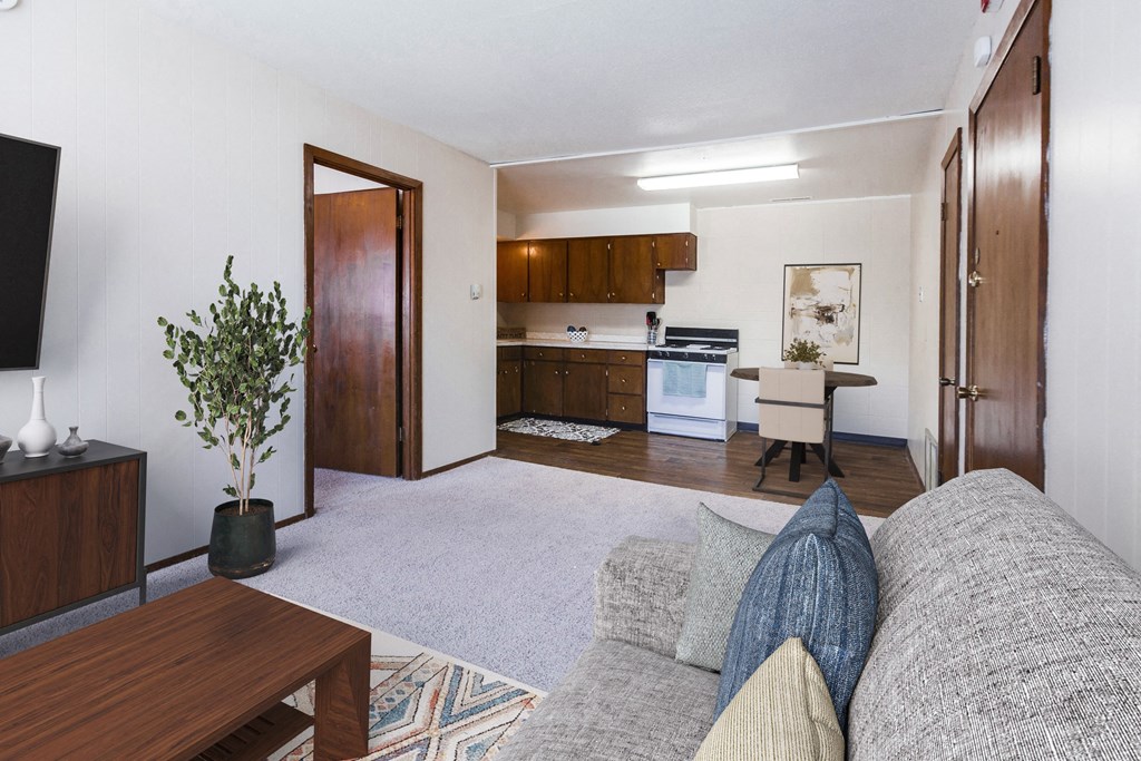 Grand Forks, ND Louise Apartments. A living room with a couch, coffee table, and the dining room and kitchen in the background.