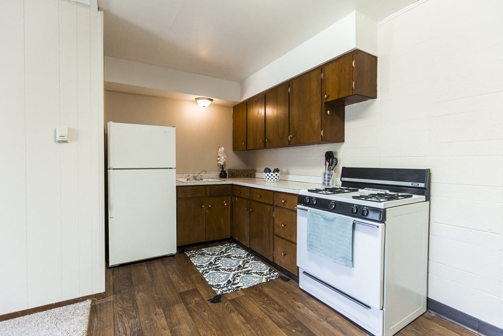 Grand Forks, ND Louise Apartments. A kitchen with white appliances and wooden cabinets